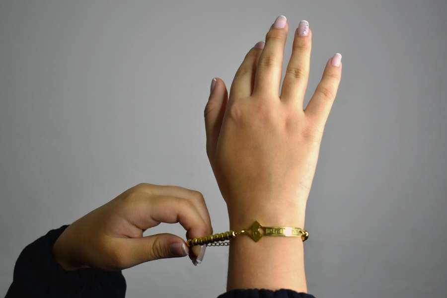 Une main ajuste délicatement un élégant bracelet manchette doré sur un poignet fin.