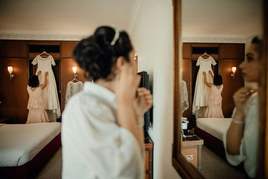 Une mariée se prépare dans sa chambre tandis qu'une proche touche sa robe de mariée dans le cadre des préparatifs de mariage.