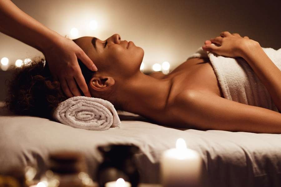 Jeune femme détendue profitant d'un massage de la tête lors d'une séance de spa dans une ambiance tamisée.