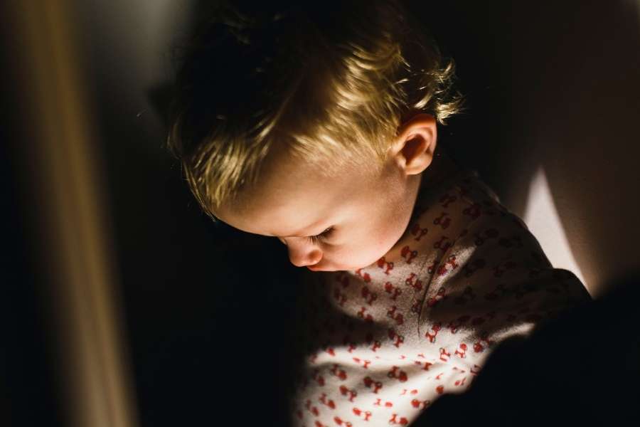 Gros plan d'un tout-petit aux cheveux blonds éclairé par une source lumineuse dans l'obscurité.