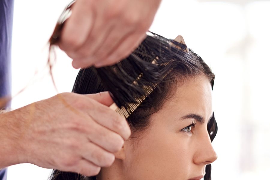 Un coiffeur peigne et soulève les mèches de cheveux humides d'une cliente en salon.